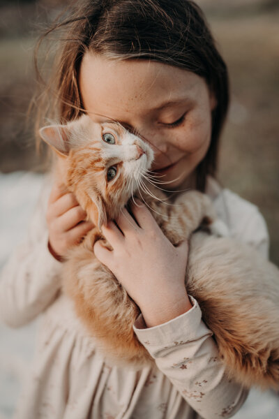 A young girl cuddles her barn cat on their family farm outside of denver colorado while she smiles.