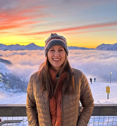 Molly Davis standing in front of an Alaskan winter sunset in the mountains