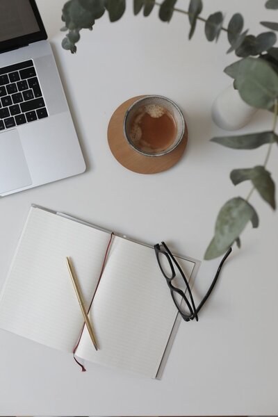 Open notebook, gold pen, glasses, coffee, and laptop on a clean desk—capturing a calm and focused work session vibe