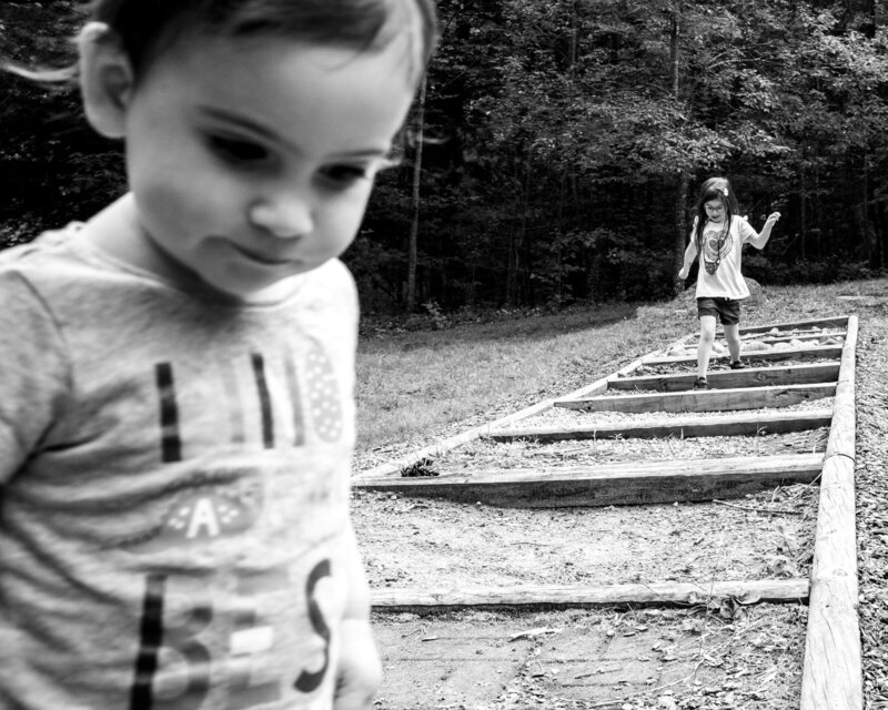 Black and white photo of a little girl standing on a wooden walkway.
