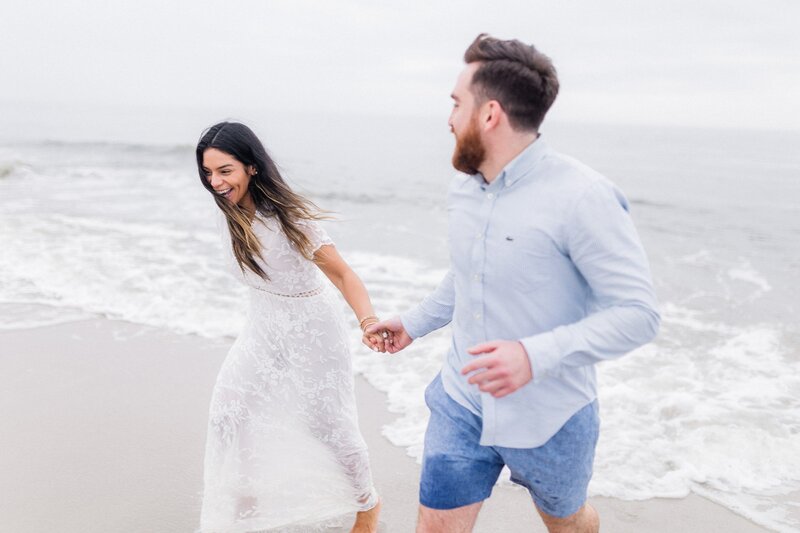 Groom to be holding bride to be with their feet in the water in Cape May Beach