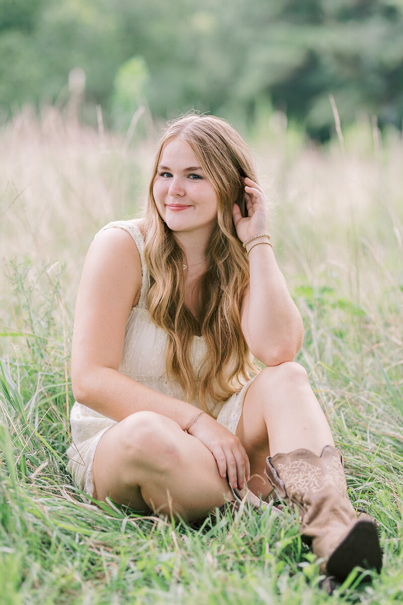 Outdoor senior portrait of a high school girl sitting in tall grass wearing a white dress, captured by Raleigh Senior Photographer Lindsey Lambert Photography.