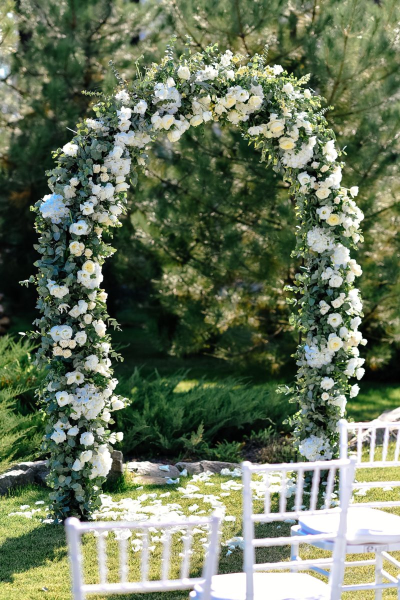 A stunning wedding ceremony arch adorned with lush florals against a backdrop of green grass, creating a picturesque scene of natural beauty and elegance.