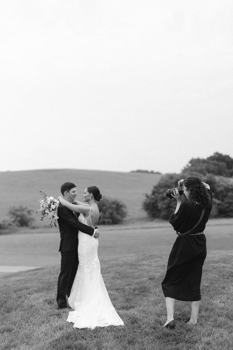 Black and white image of Victoria Barclay, photographer at Through Victoria's Lens, taking photos of a bride and groom