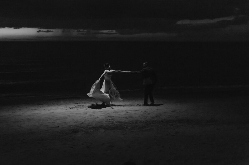 Cinematic black and white photo of a couple dancing on the beach at night, captured by Rainstorm Photo & Video in a romantic, cinematic style.