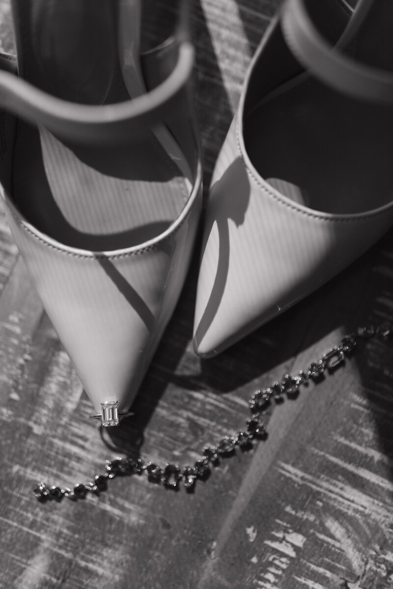 A high-end editorial-style black and white wedding detail shot featuring designer bridal heels and a sparkling engagement ring, embodying luxury and elegance.