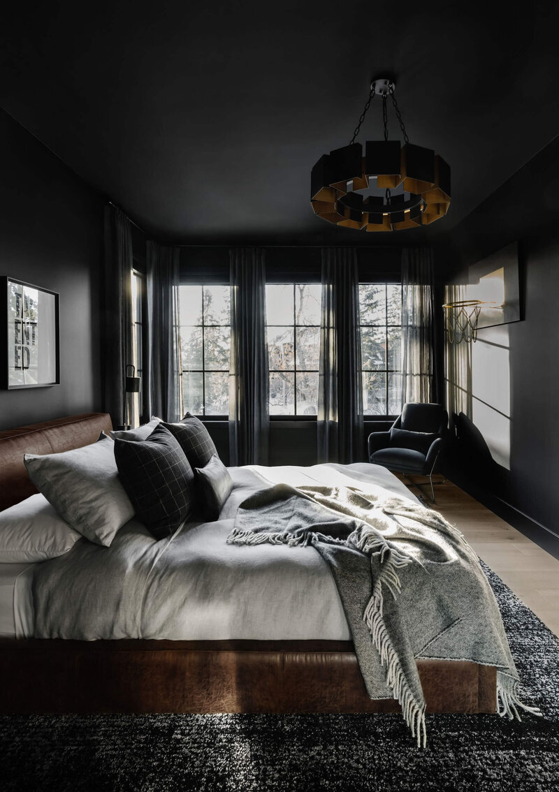 A dark and moody bedroom with black paint, cognac leather with grey linen bedding. 
