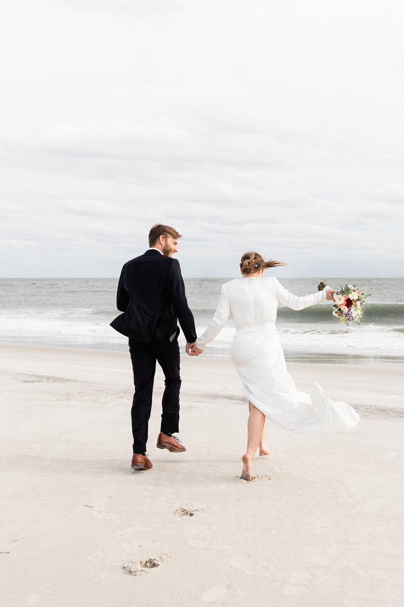 Photo of bride and groom laughing and holding hands on the beach during their Peter Shields Inn wedding in Cape May NJ