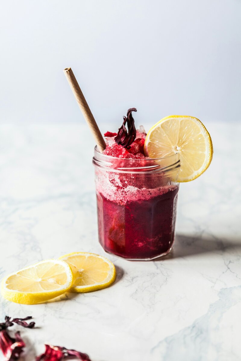 Bright red icy juice drink in a clear glass with a lemon slice