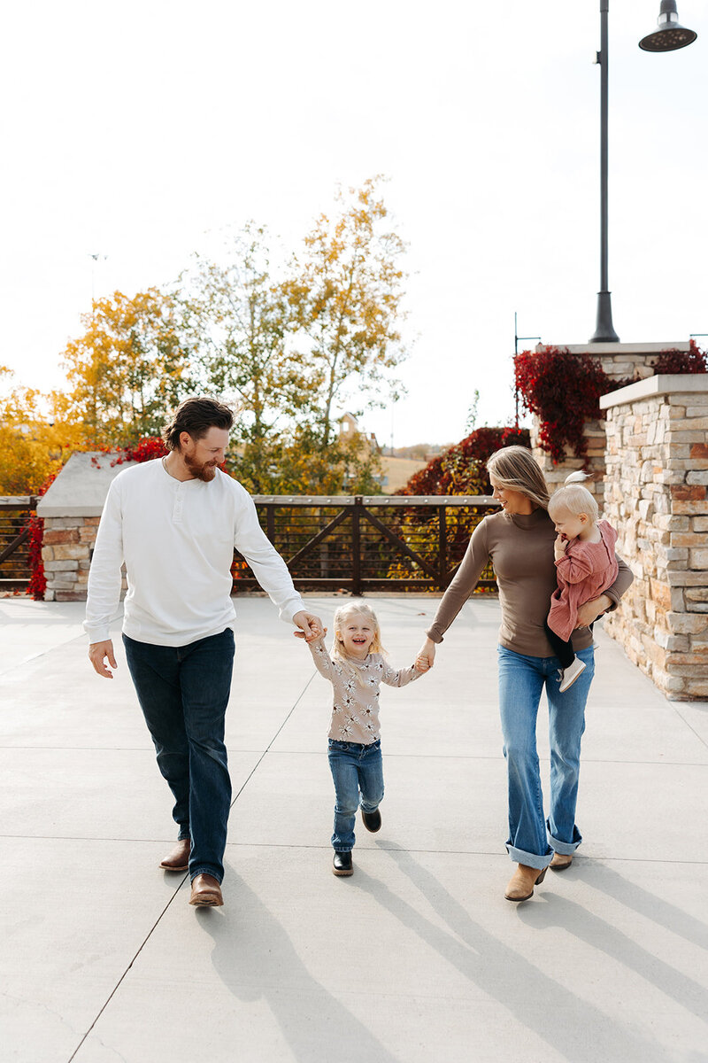 Parents swing their song by the hands across cobblestone sidewalk