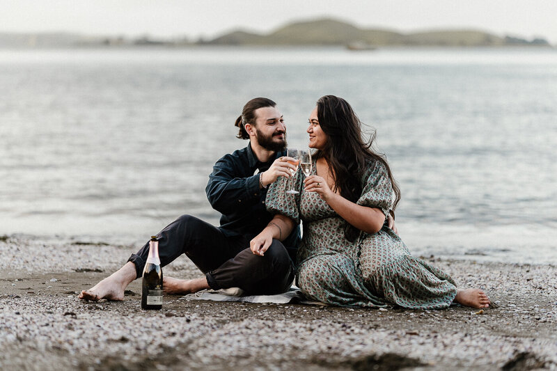 Engagement photography session on the beach in Auckland with a newly engaged couple and a bottle of champagne.