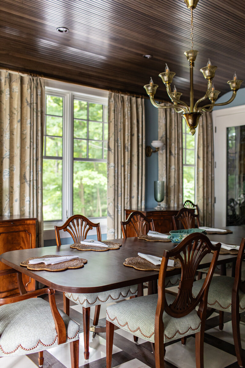 A luxurious dining room featuring rich wood ceilings, gold finishes, and an abundance of wood accents. The space is complemented by patterned curtains and custom flooring, creating a warm and inviting atmosphere.