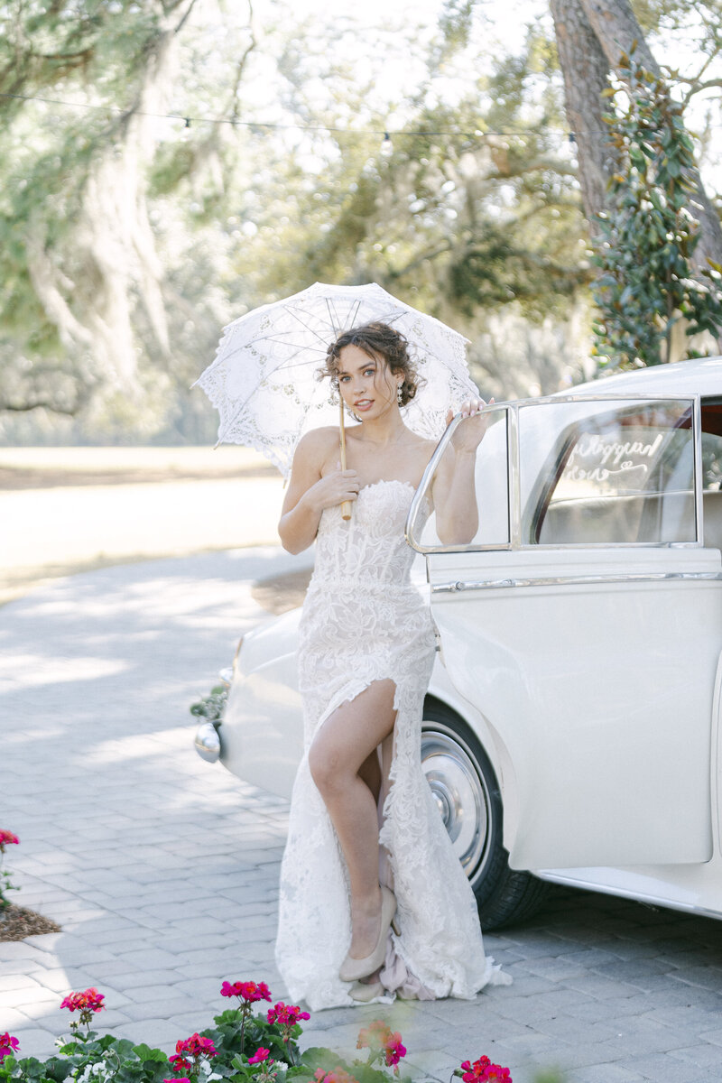 bride holding a parasol outside of a vintage bentley at hewitt oaks wedding venue captured by savannah wedding photographer magnolia west photography