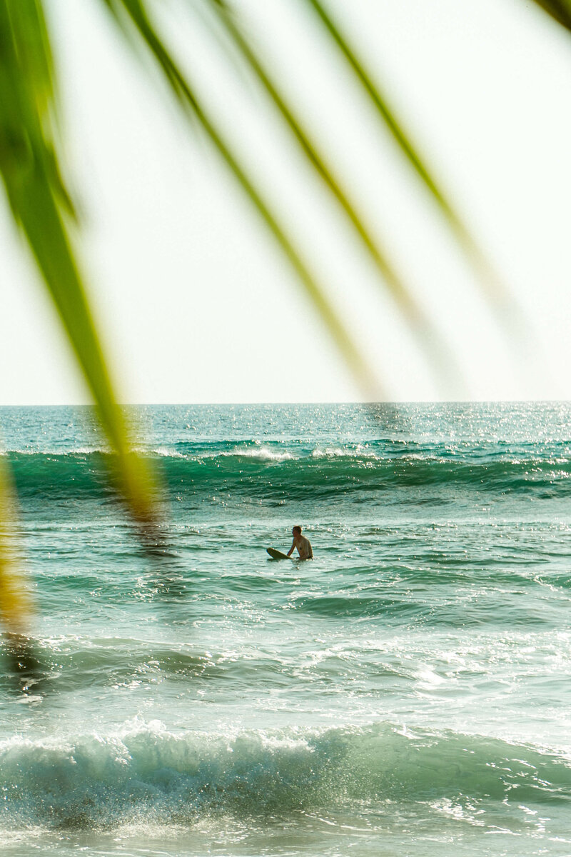 Surfer sitting on surfboard with wave in the back