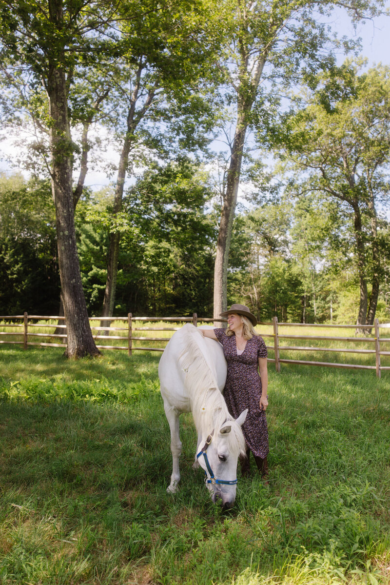 Leiko standing beside a white horse in a sunny Berkshire pasture, guiding equine-assisted healing work