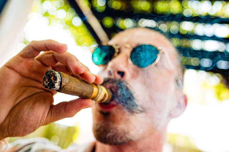 A groom with a huge mustache smoking a cigar before the wedding wearing sunglasses 