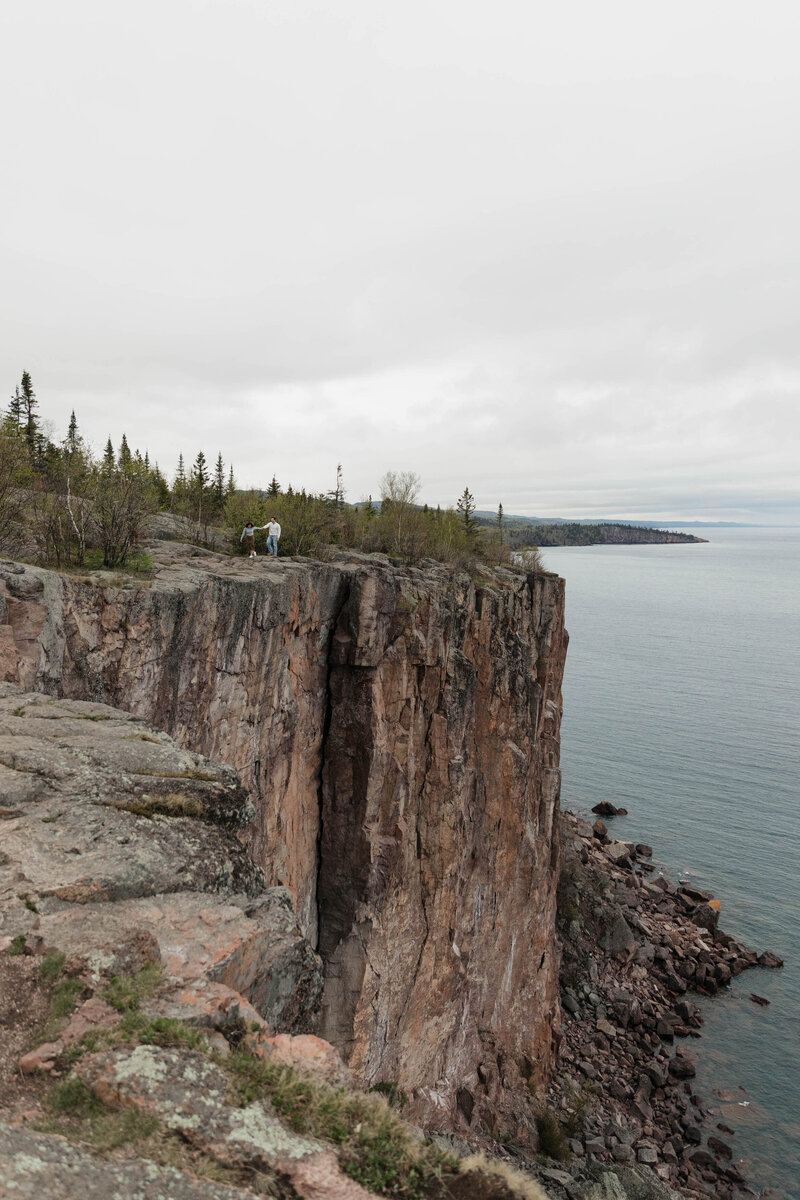 A couple holding hands and walking along a cliffside