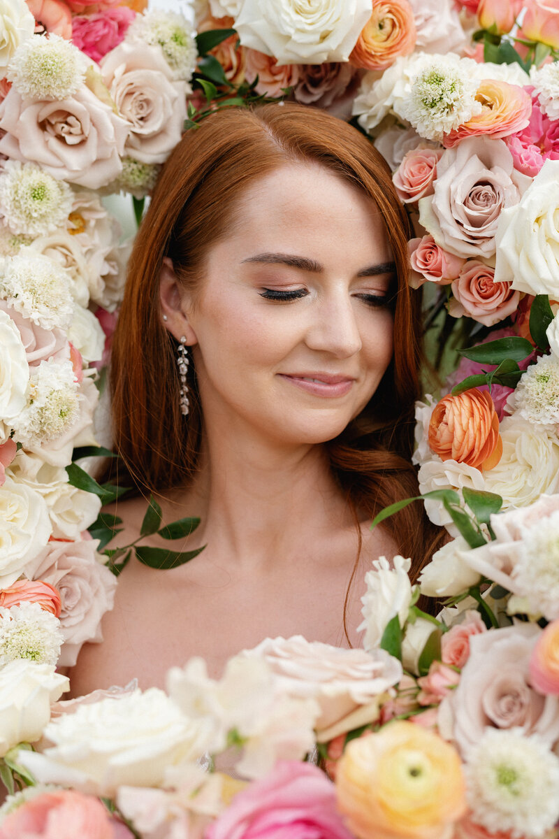 Bride nestled in a romantic floral frame of blush, peach, and cream blooms, representing Bloom Bar’s custom wedding floral arrangements in Austin.