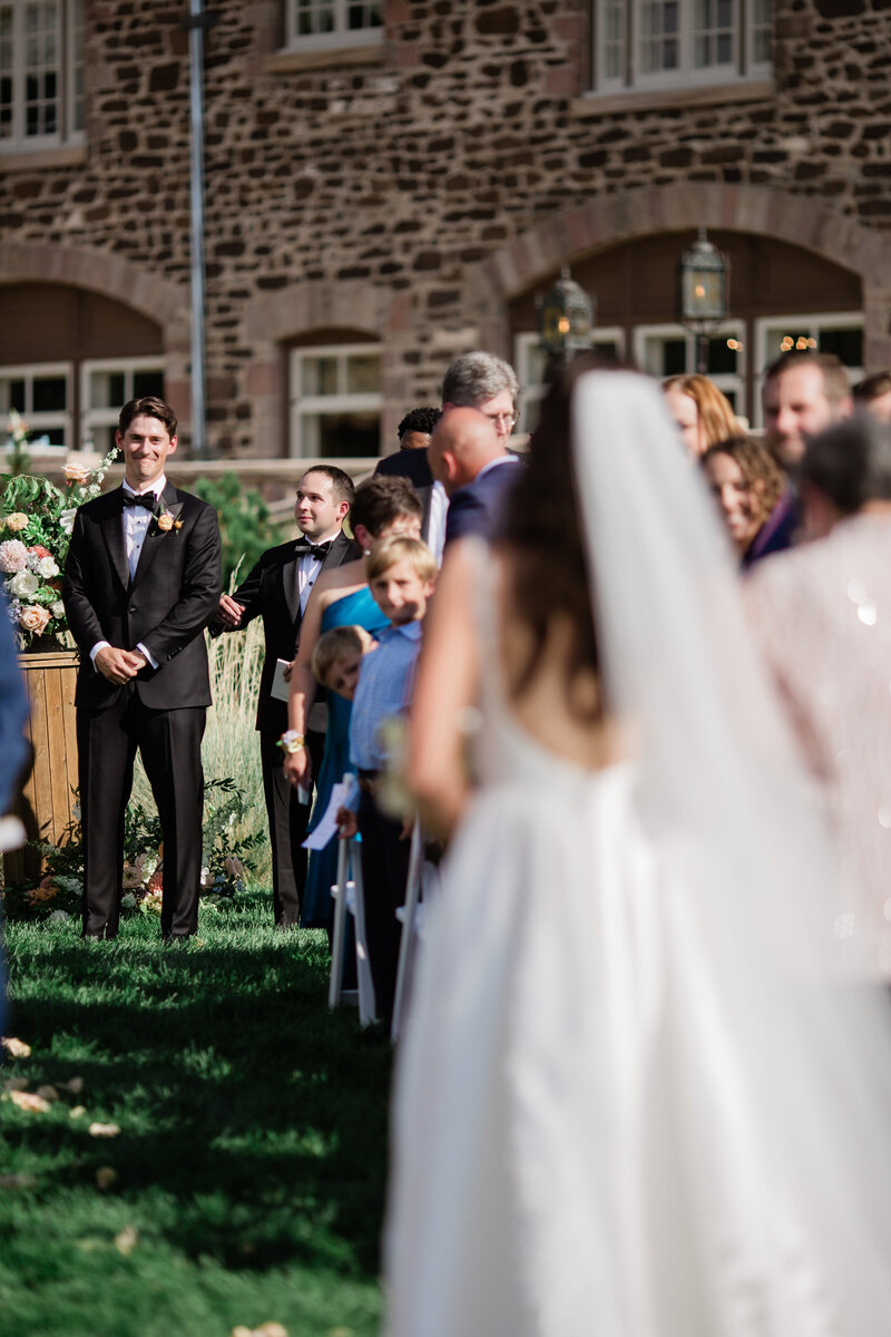 Groom watching bride walk down aisle with a smile