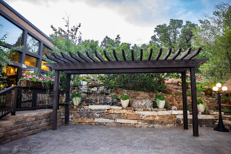 Outdoor Patio with dark wood Pergola and Waterfall backdrop for outdoor wedding ceremonies at Craftwood Peak Wedding Venue in CO