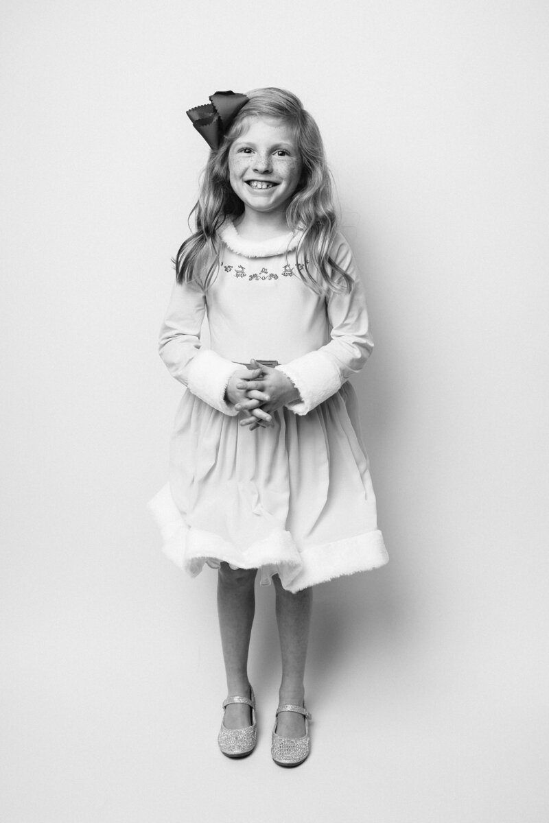 Black and white image of girl in Elf Character Jovie inspired outfit. Girl has a friendly smile and is holding her hands togther.