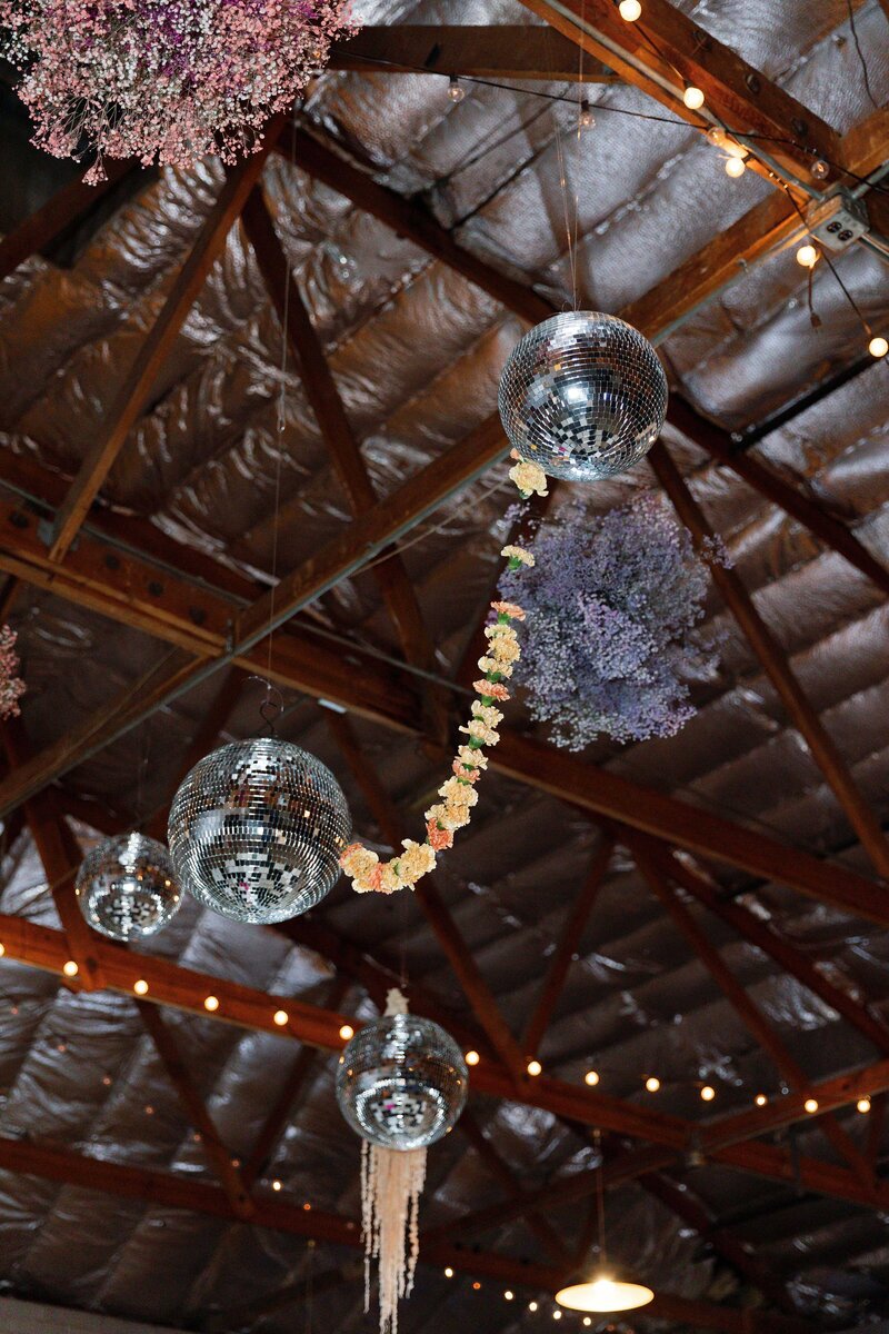 Disco balls and floral installation hang from ceiling above wedding dance floor.