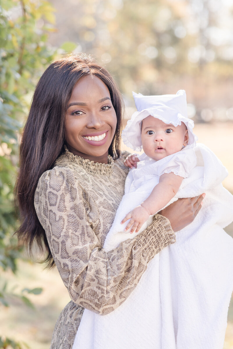 Mother holding baby in a white bonnet smiling.