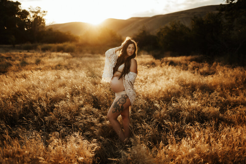Pregnant mother in nude underwear in a field at golden hour.