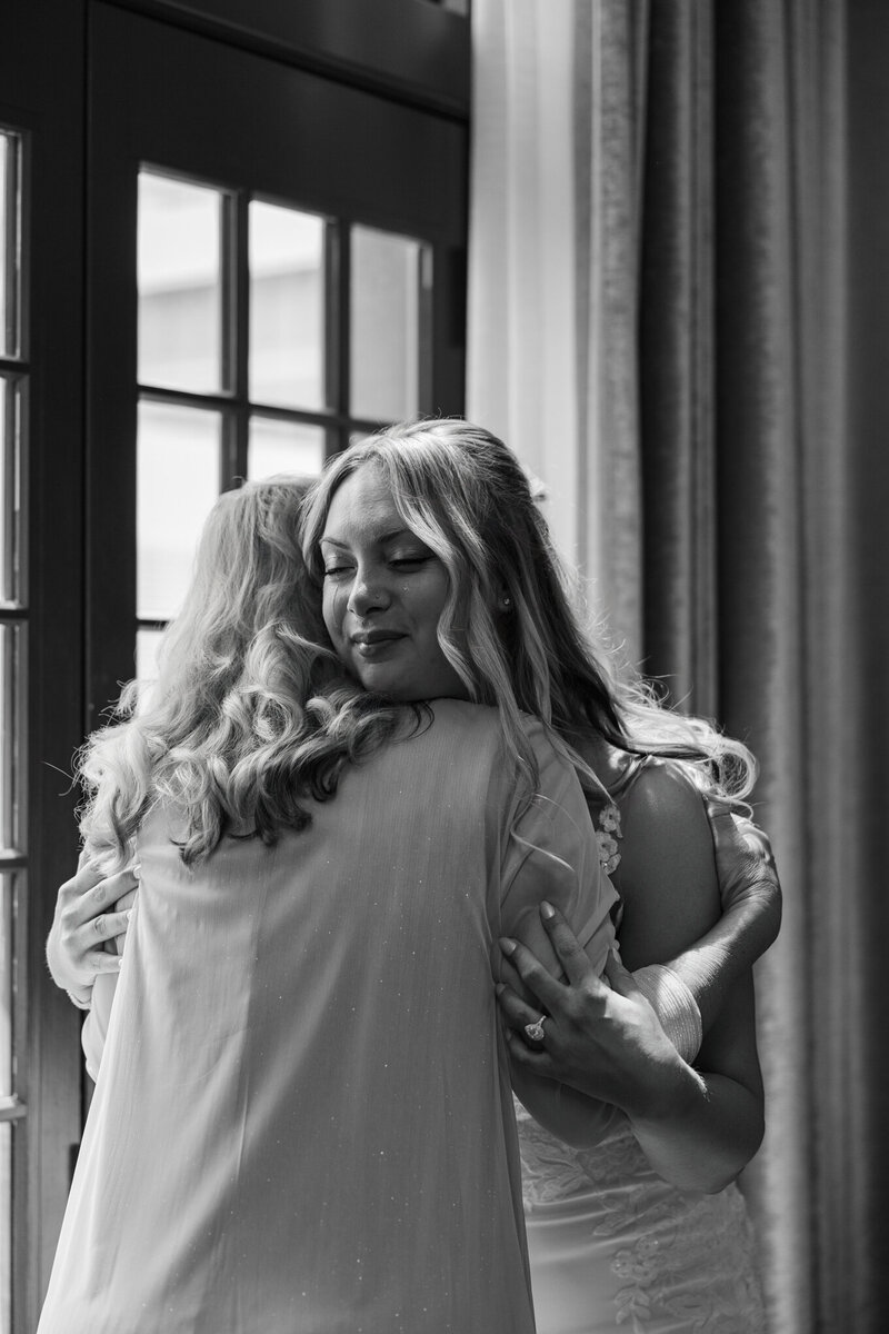 Emotional, documentary-style wedding photography of a bride and her mother hugging and crying as she gets ready photographed in black and white by Claire Katan Creative.
