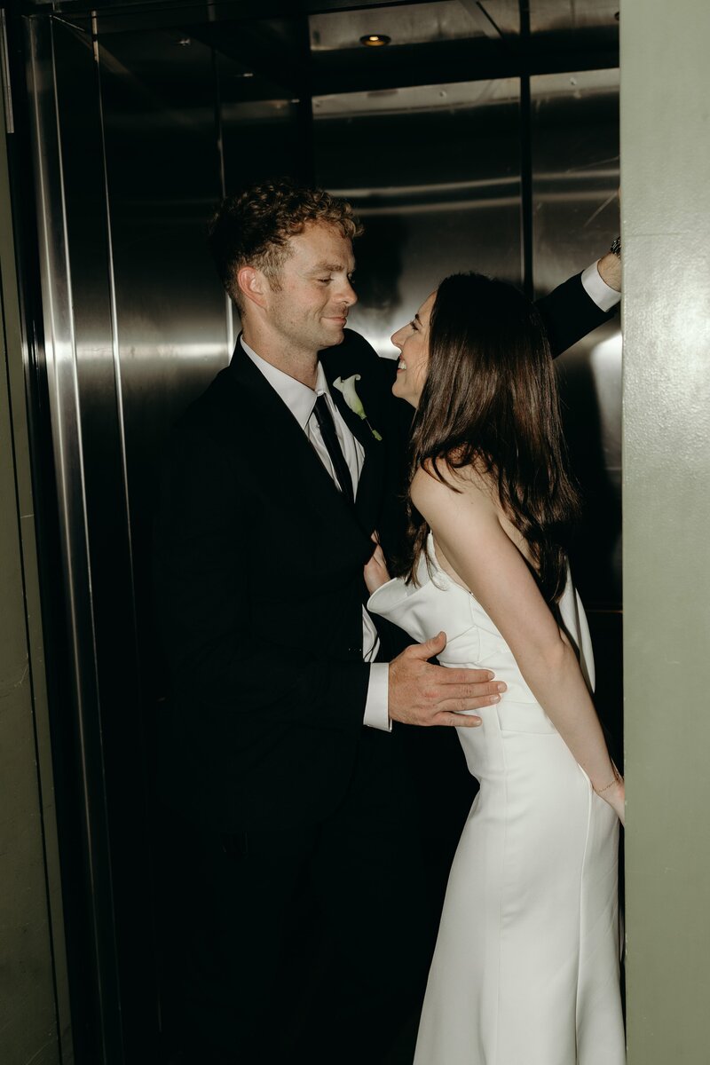 A classy direct flash photo as a wedding couple snuggles close in n elevator