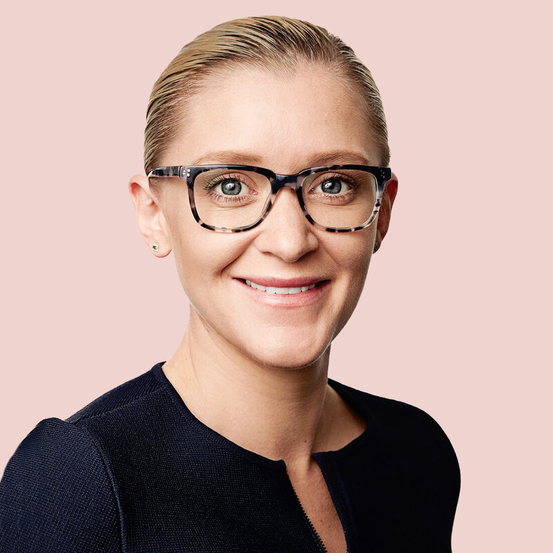 Smiling corporate woman with glasses against pink backdrop.