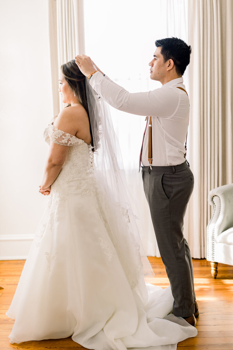 brides brother helps her put on her veil