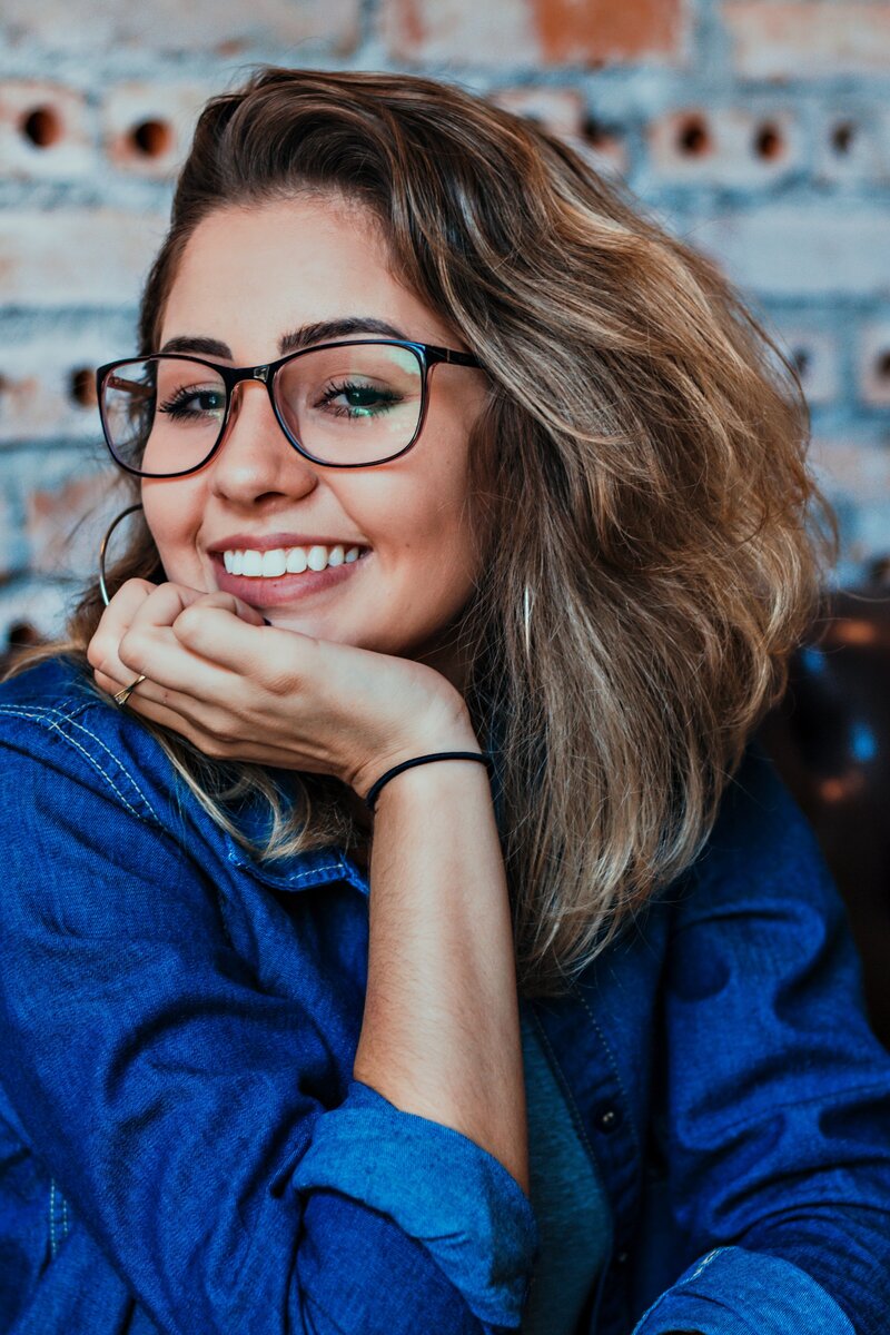An image of a smiling woman wearing glasses and a jean shirt.