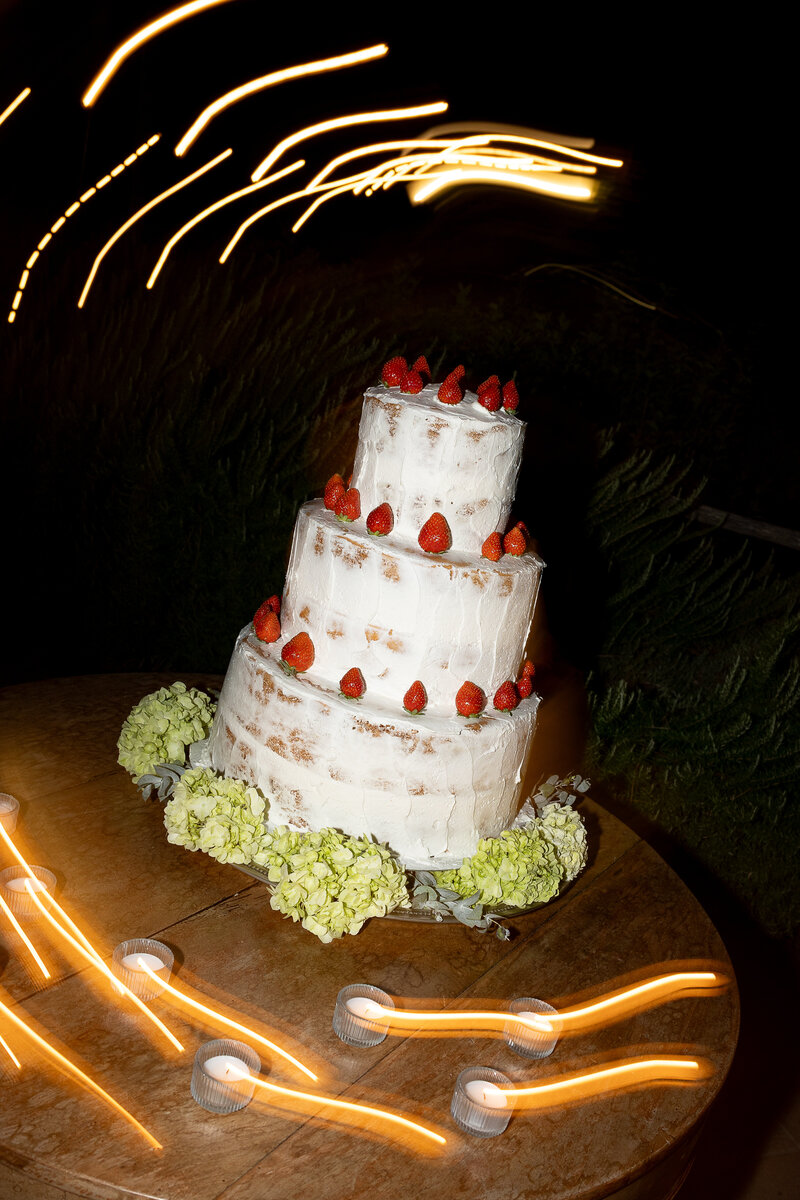 Blurry three-tier white wedding cake lightly decorated with clusters of red strawberries. 
