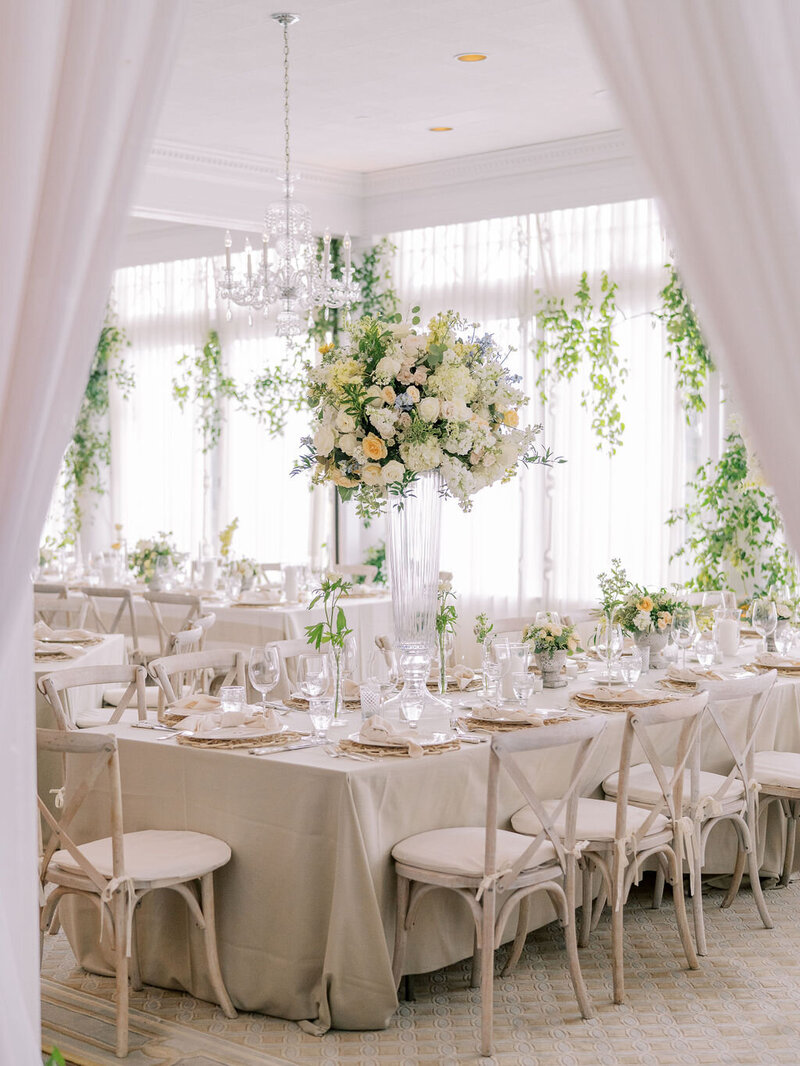 Elegant wedding reception room with neutral tones, tall floral centerpieces, and greenery accents.