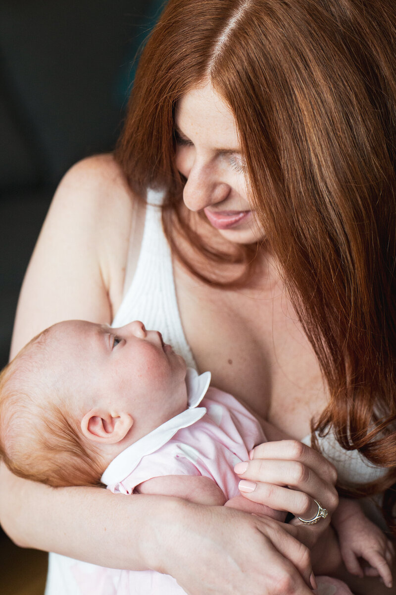 A new mom with beautiful red hair snuggles her baby girl in a pink onesie
