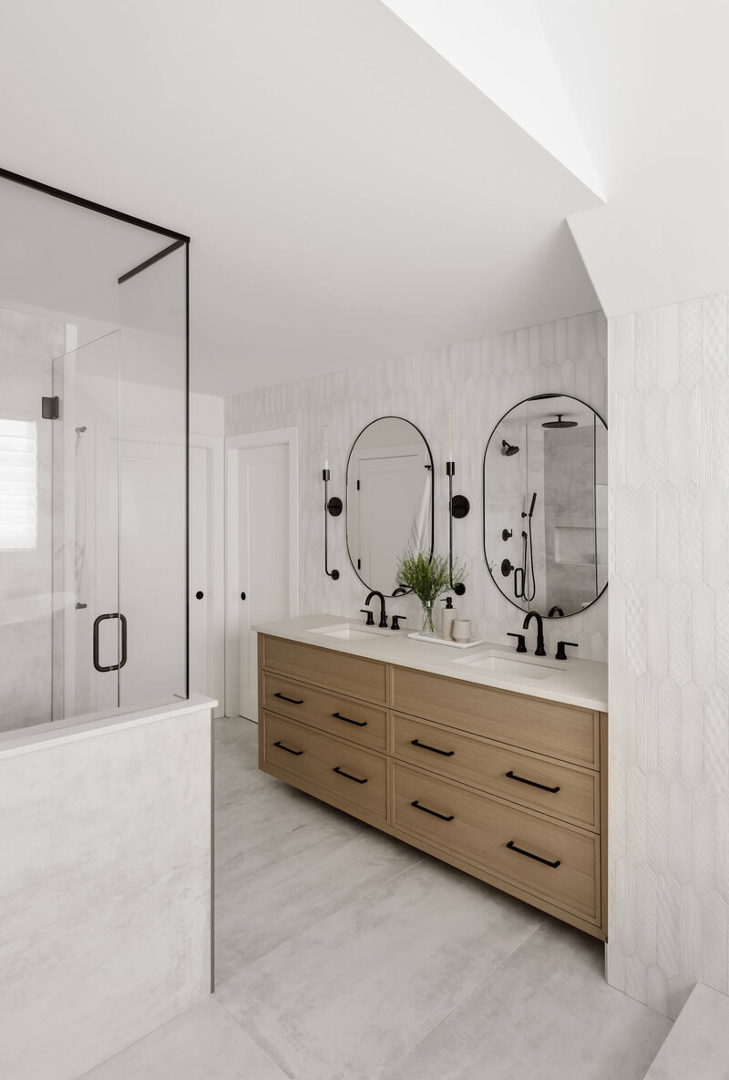 An ensuite renovation with grey and white tile and white oak skinny shaker cabinets and black hardware.