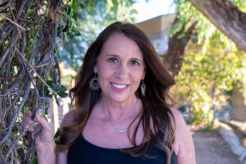 Smiling woman standing beneath a leafy garden arch, photographed outdoors by Vyrl Photo, representing Tucson brand photography.