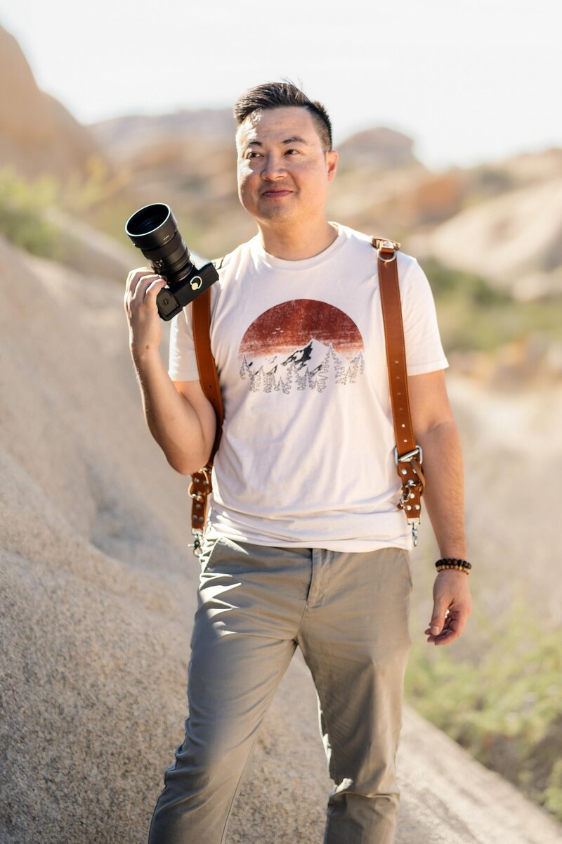 Peter 3 Nguyen from Peter 3 Photography, standing with a camera in Joshua Tree Jumbo Rocks for elopement photography and adventurous intimate weddings.