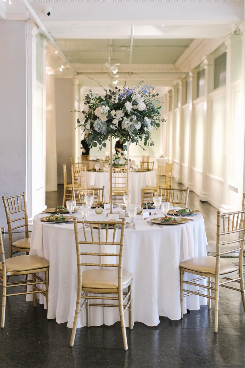 A white table with gold plates and chairs and a bouquet of purple and white flowers in the center