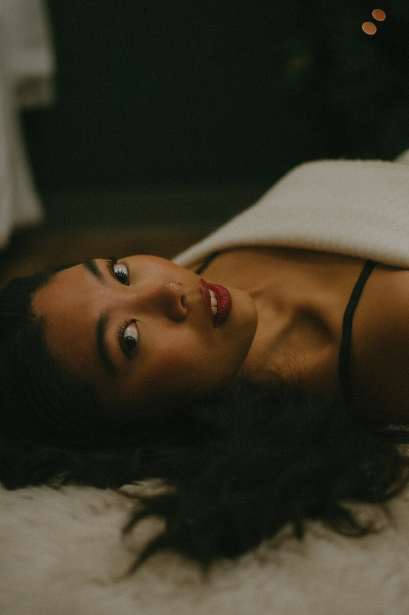 Woman lounging on a dark blue velvet wall in a two piece cut out dress.