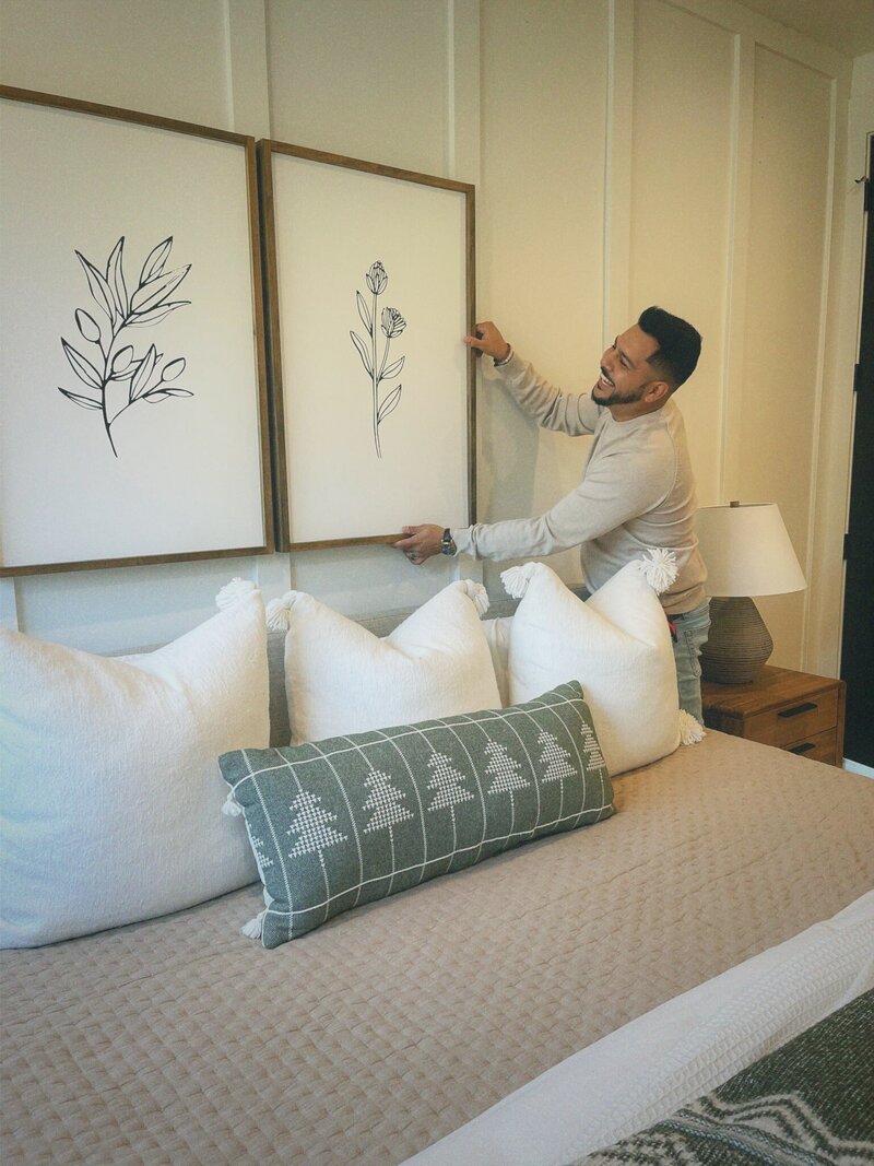 interior designer man is hanging up abstract wall art in a newly designed farmhouse bedroom space