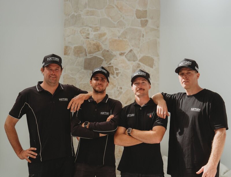 A dynamic team from NXTgen Construction standing together confidently in front of a textured stone wall, showcasing their commitment to craftsmanship and excellence.