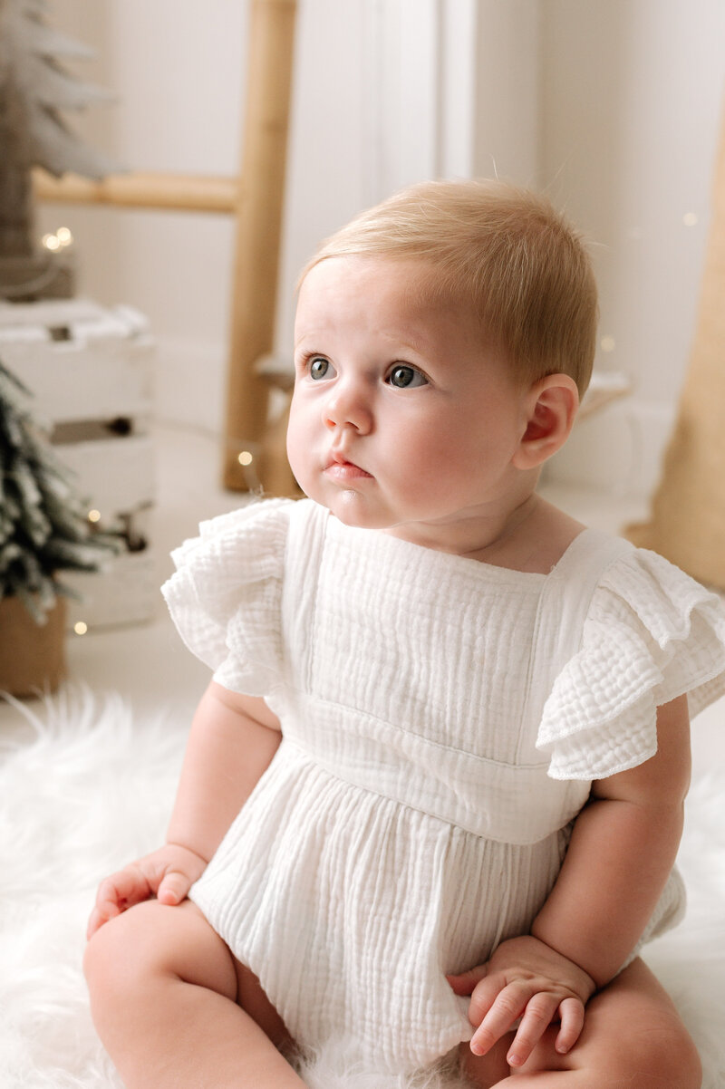 Little girl smiling sitting on a white stool infront of a christmas tree at a christmas family photoshoot in Billingshurst