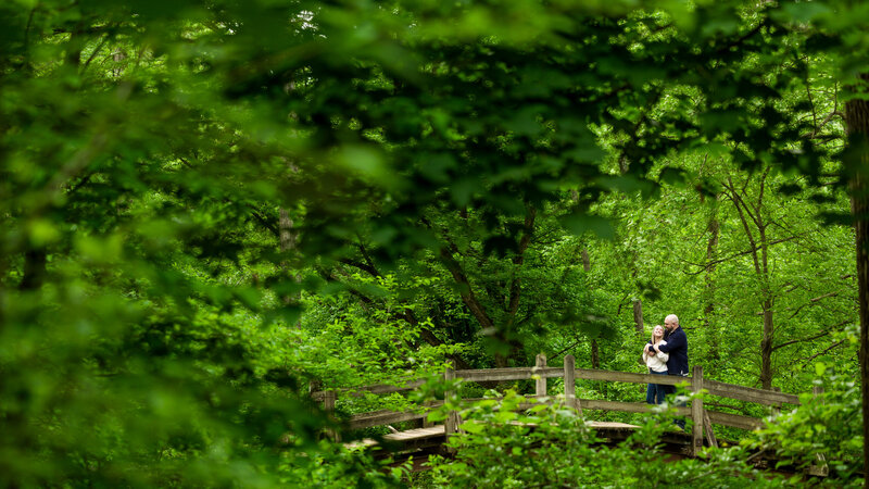 Couple standing on a wooden bridge surrounded by lush trees at Valley Forge National Historical Park, embodying their love for the outdoors.