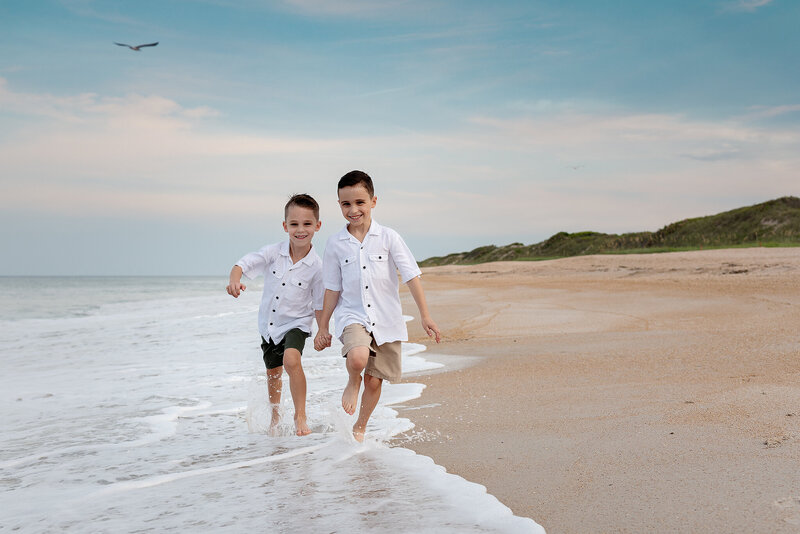 Brothers in white shirts running along shoreline at Guana Reserve Beach in Ponte Vedra, FL.