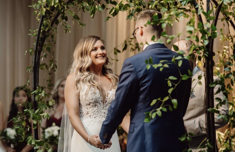 bride and groom holding hands under greenery  arch