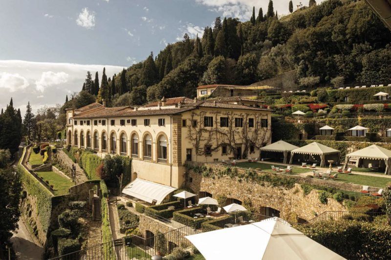 Bird's eye view of Borgo Santo Pietro, a refined Italian country borgo with classic stone buildings spread out between cypress ree lanes, gardens and forests