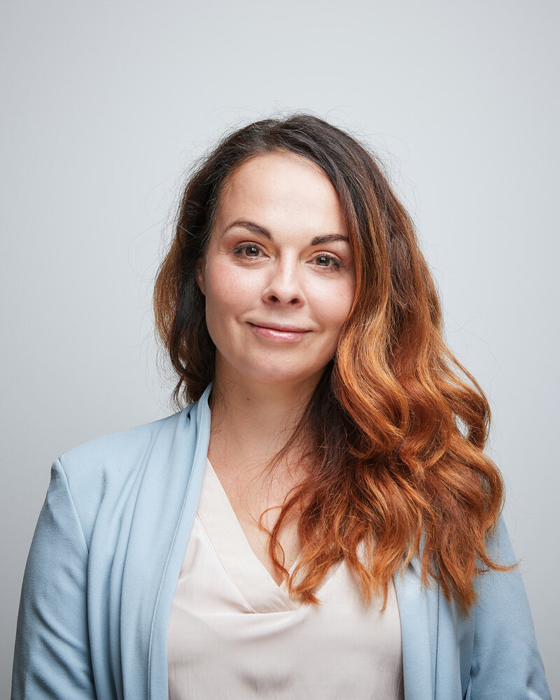 Lady's face, shoulder, and neck against a wall indoors. Tags include human face, smile, clothing, portrait photography, and fabric.