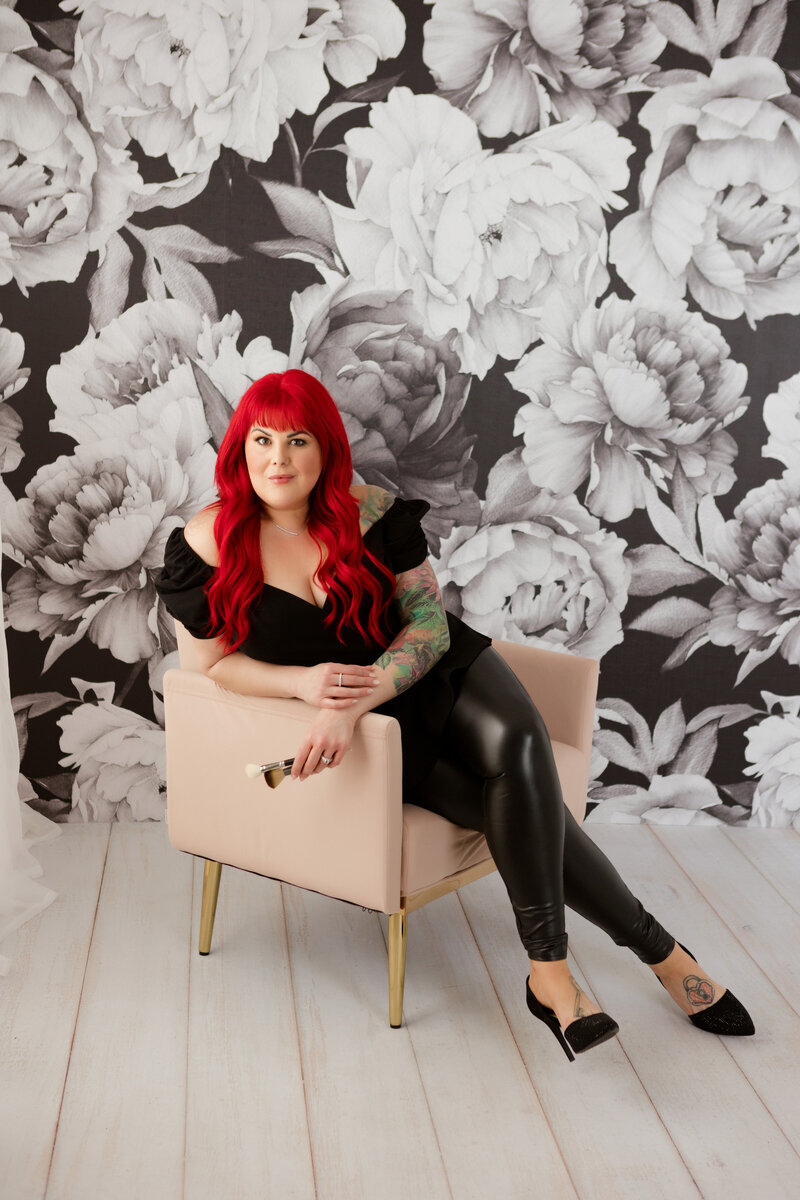 Makeup artist poses for brand photos with black and white floral wallpaper in the background